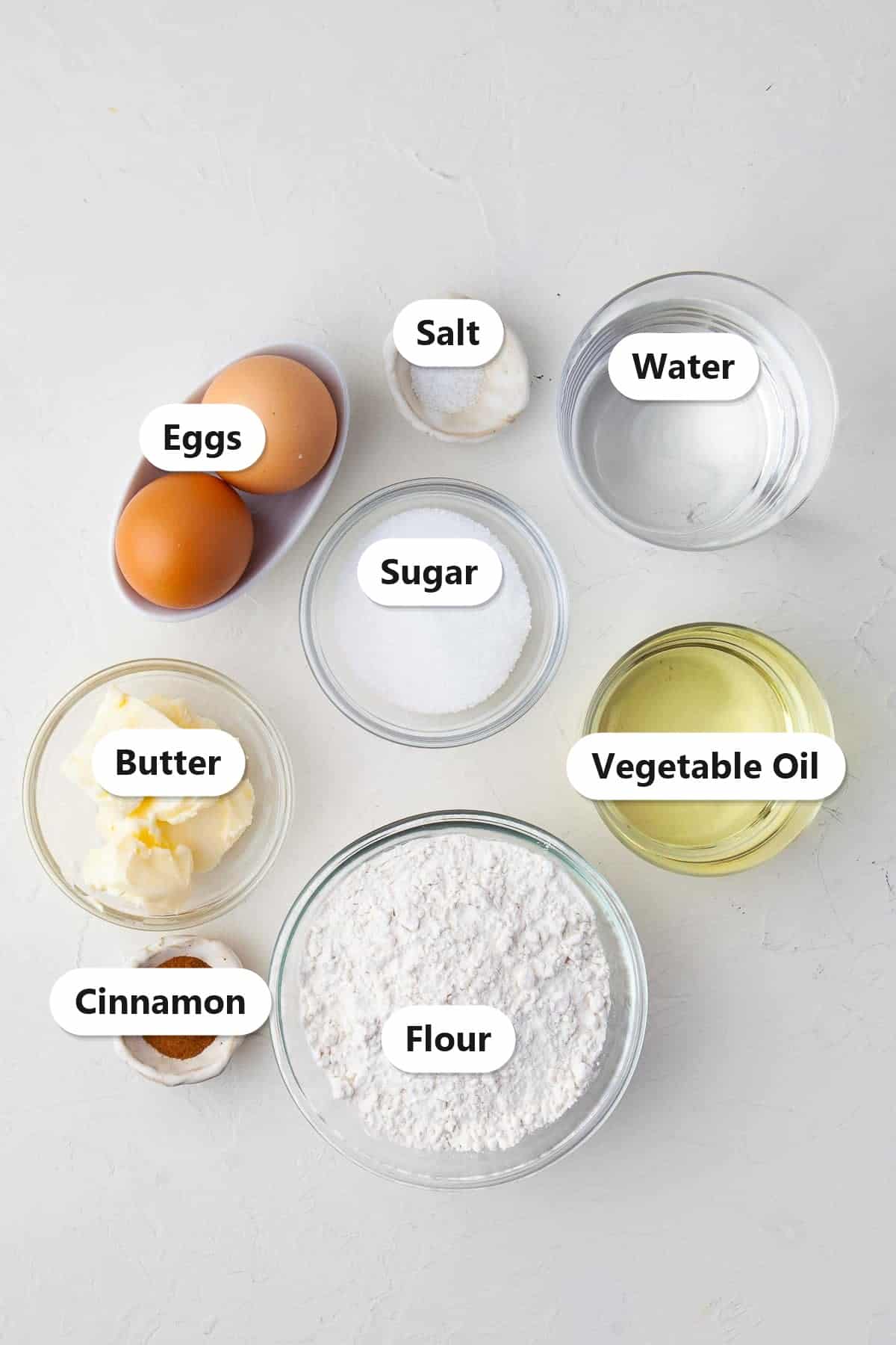 Labeled ingredients for homemade mini churros including water, butter, sugar, salt, flour, eggs, cinnamon, and vegetable oil.