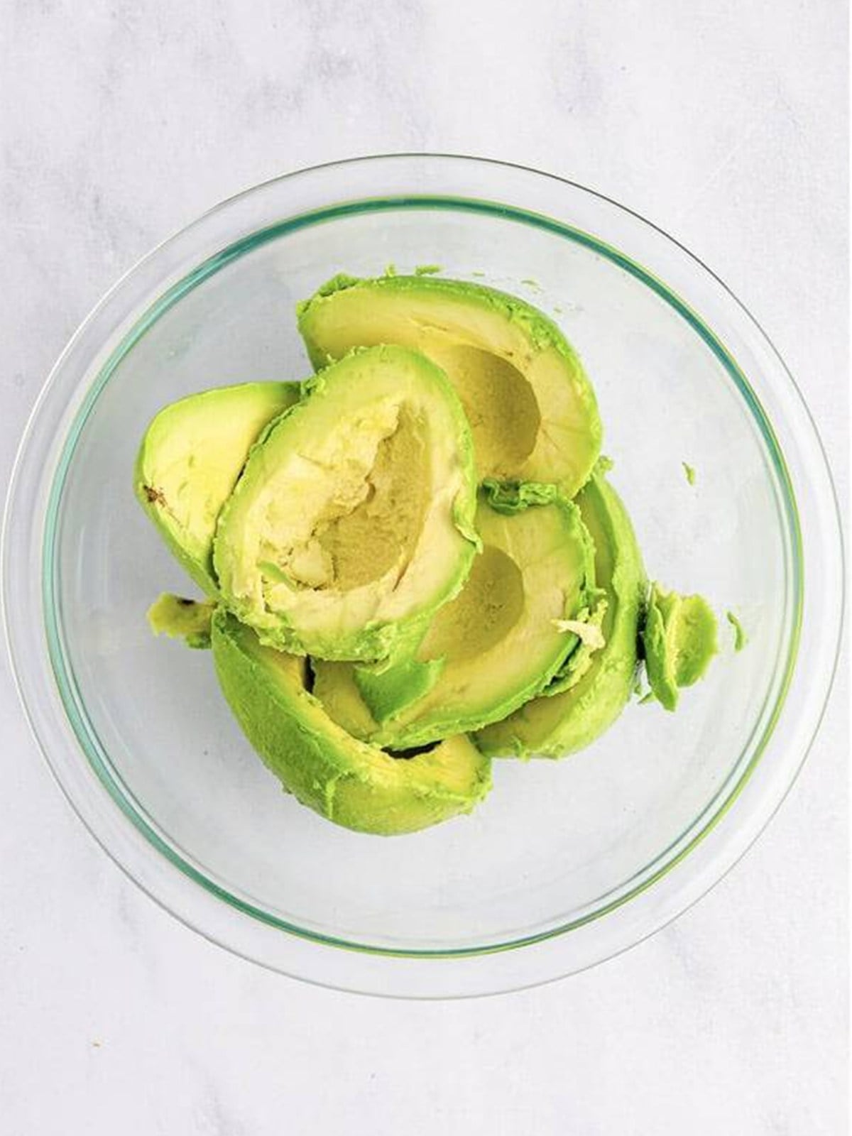 Ripe avocados mashed in a glass bowl for homemade guacamole.