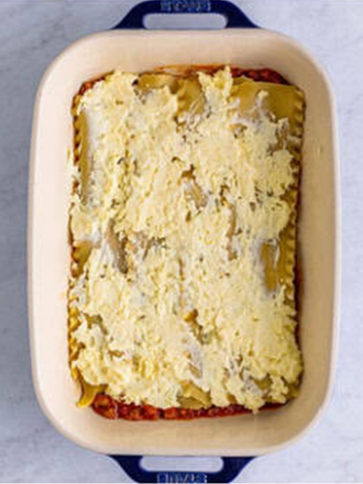 Ricotta cheese filling spread over lasagna noodles in a baking dish.