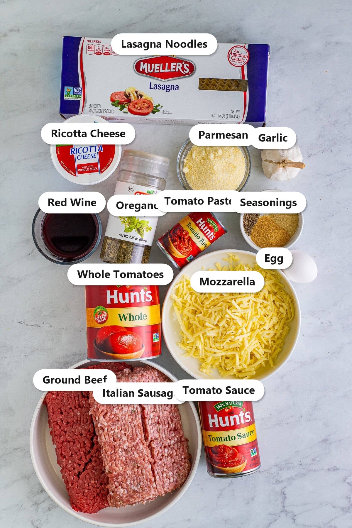 Labeled ingredients for homemade lasagna including ground beef, Italian sausage, ricotta, mozzarella, parmesan, lasagna noodles, red wine, and canned tomatoes.