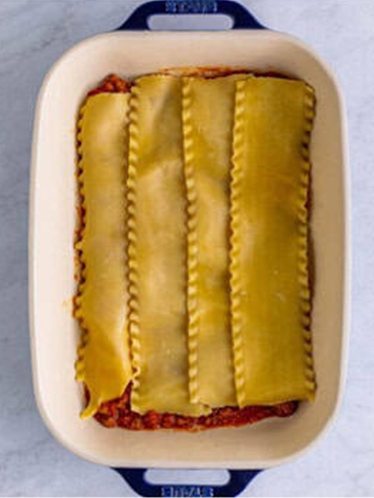 Lasagna noodles layered over meat sauce in a baking dish.