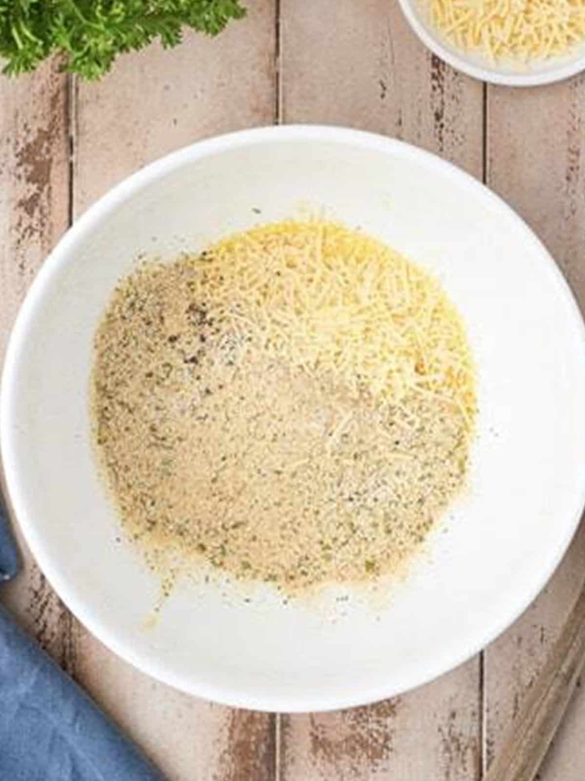 Parmesan cheese, panko breadcrumbs, and seasonings combined in a white bowl for homemade meatballs.