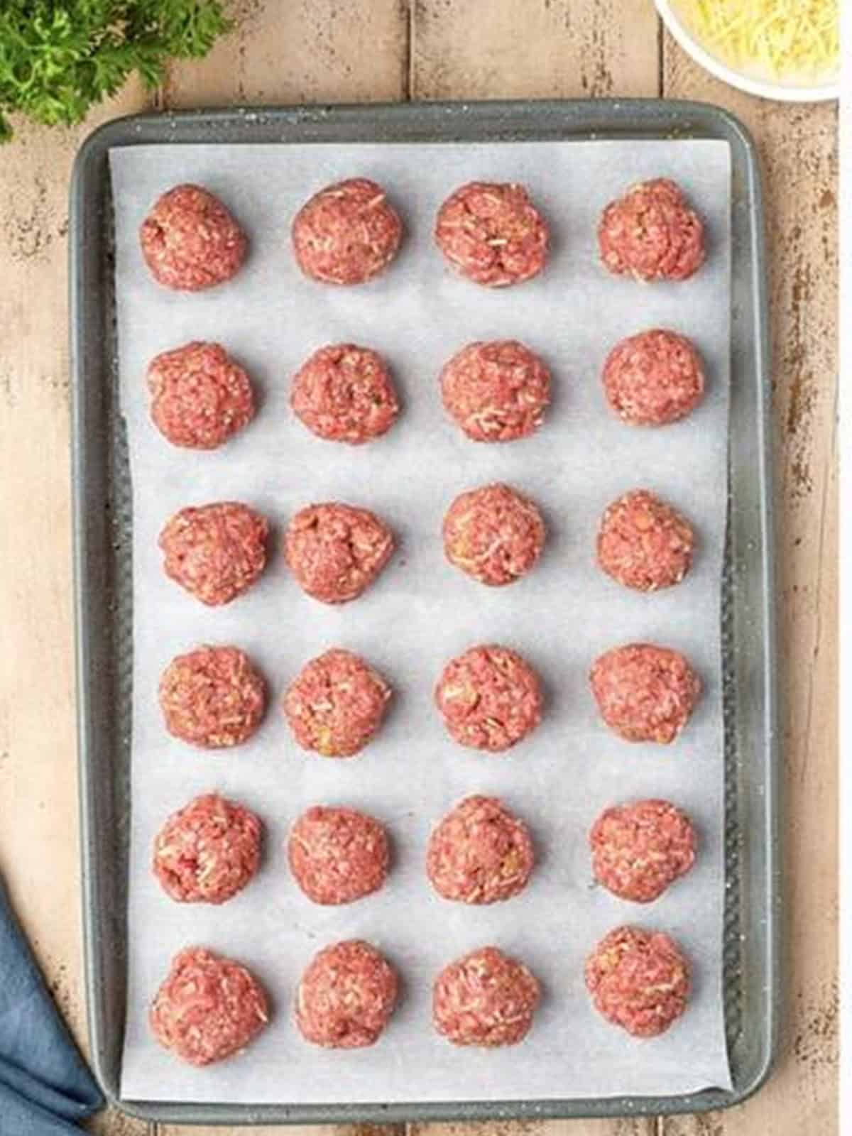 Rolled homemade meatballs lined up on a parchment-lined baking sheet ready for the oven.