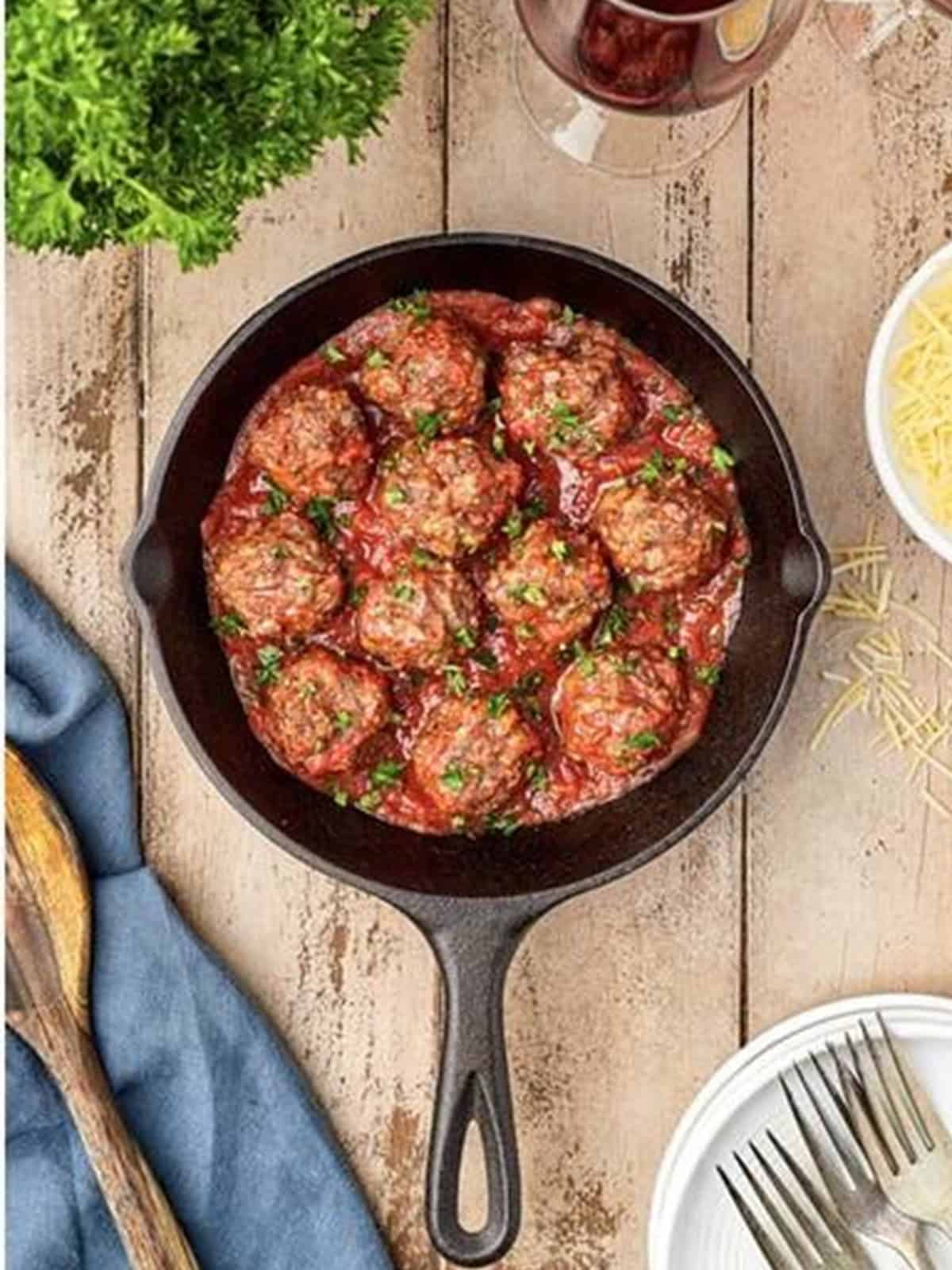 Homemade meatballs simmering in marinara sauce in a cast iron skillet.