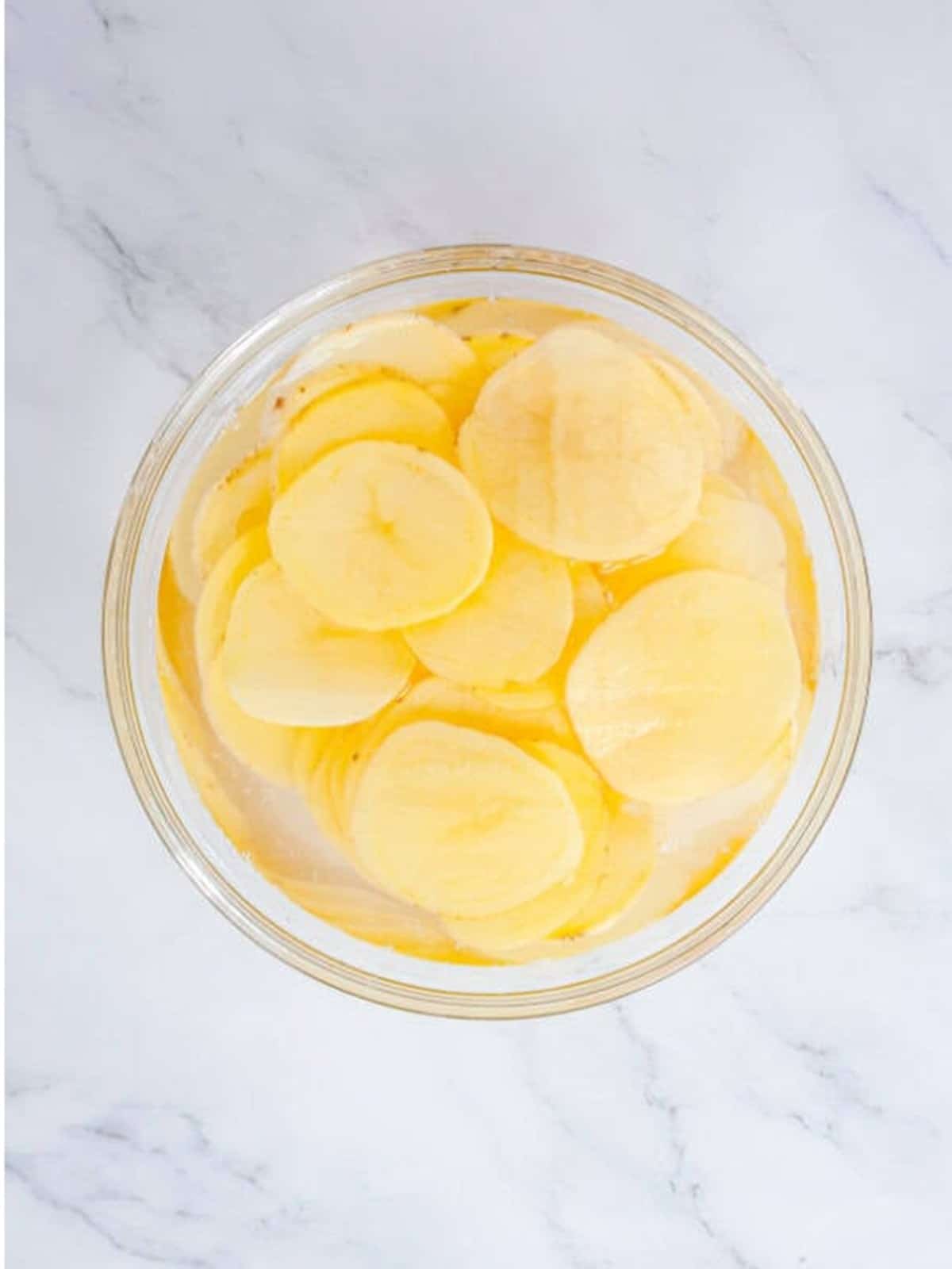 Thinly sliced potatoes soaking in a bowl of cold water to make Homemade Potato Chips.