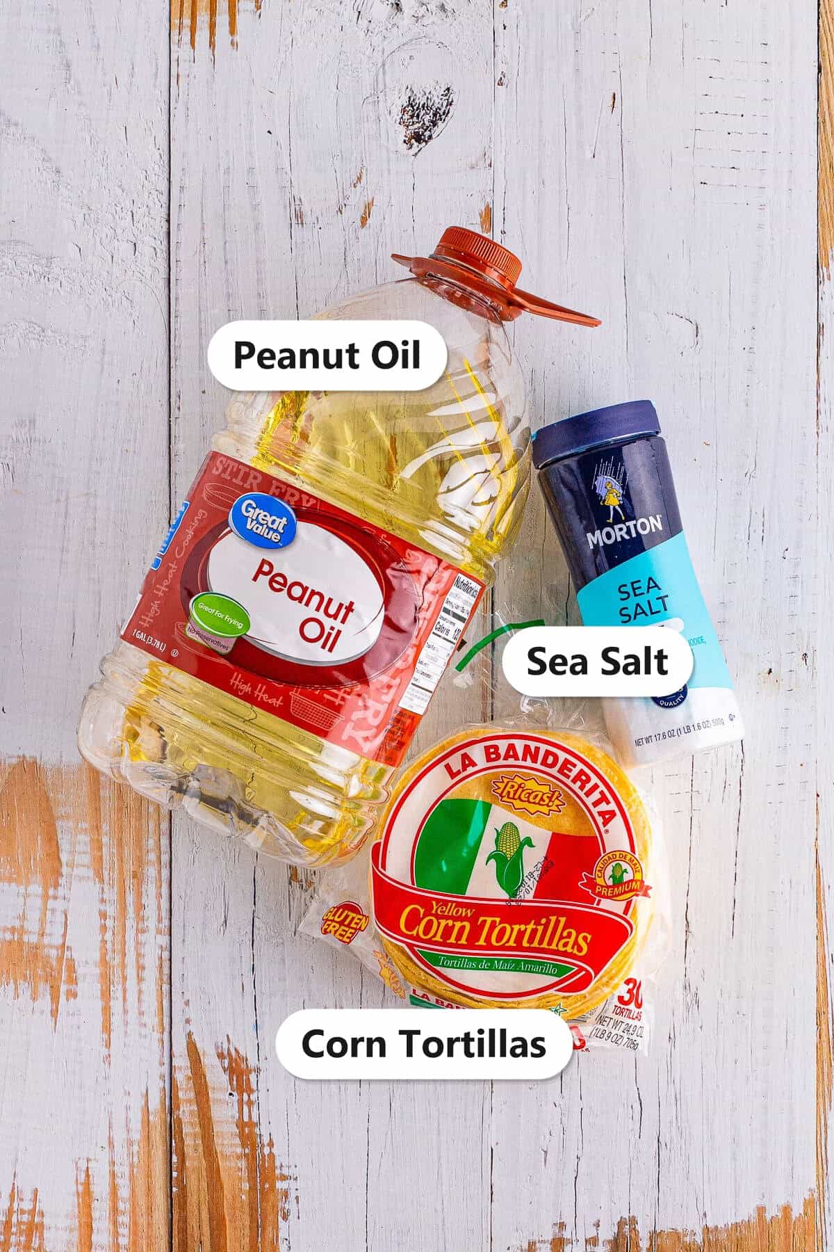 Homemade tortilla chips ingredients including corn tortillas, peanut oil, and sea salt labeled on a wood surface.