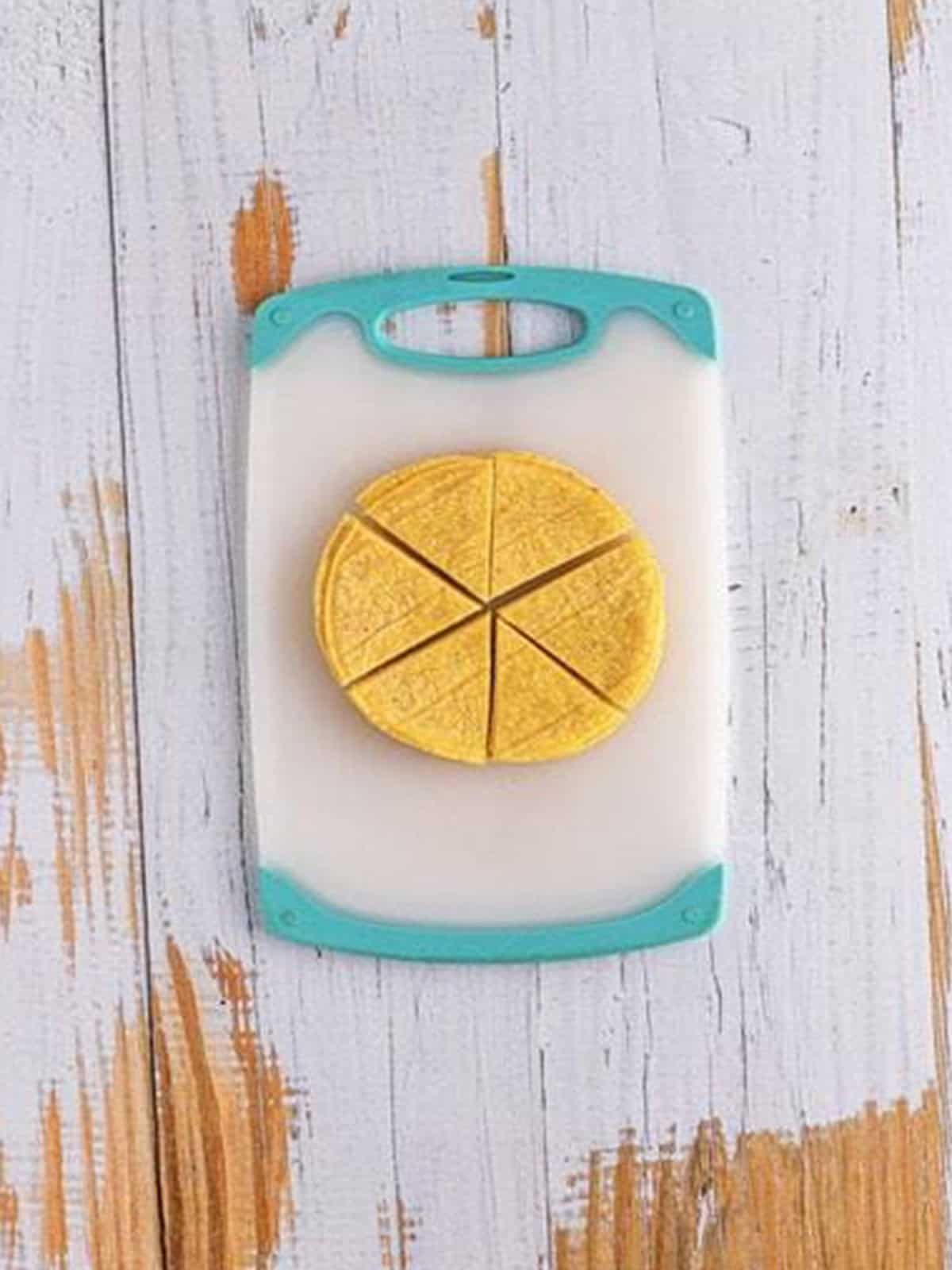 Corn tortillas stacked and cut into triangles on a cutting board for tortilla chips.