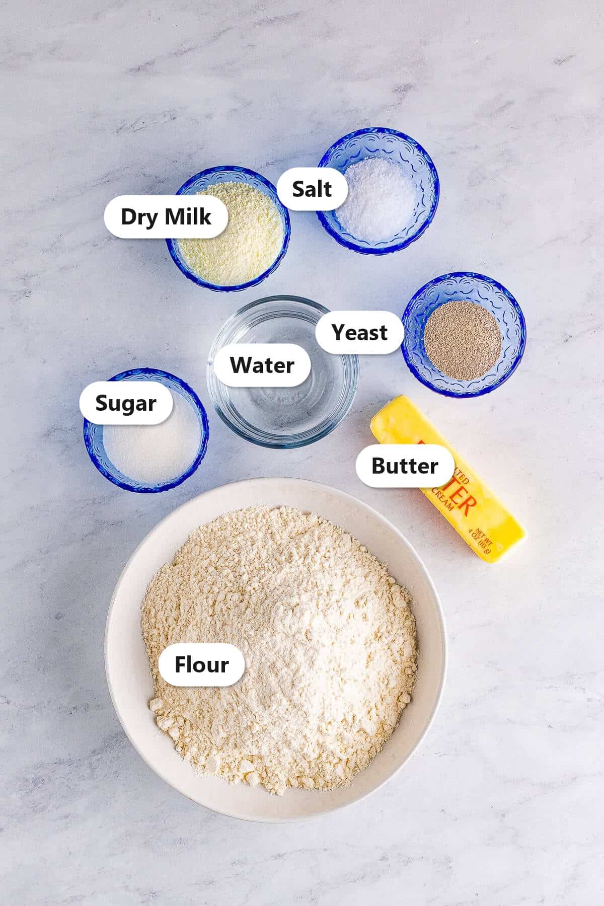 Labeled ingredients for homemade white bread including flour, dry milk, sugar, yeast, salt, water, and butter.