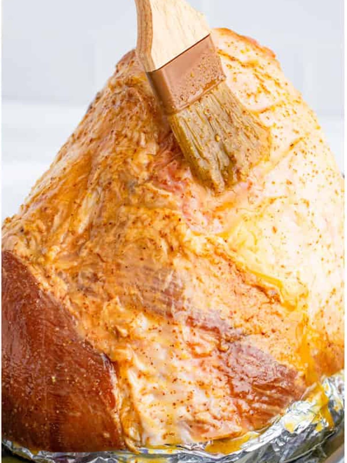 Brushing the honey mustard glaze all over the scored ham.
