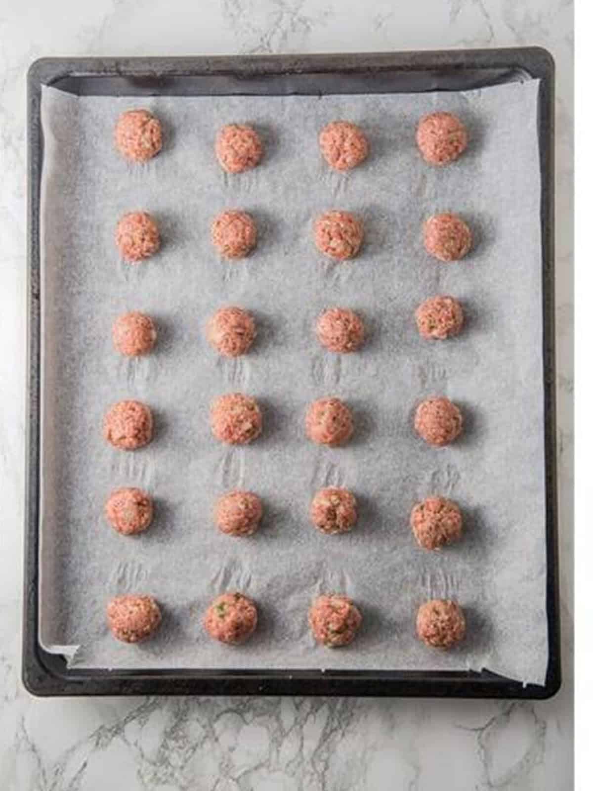 Raw honey BBQ meatballs formed and arranged on a parchment-lined baking sheet.