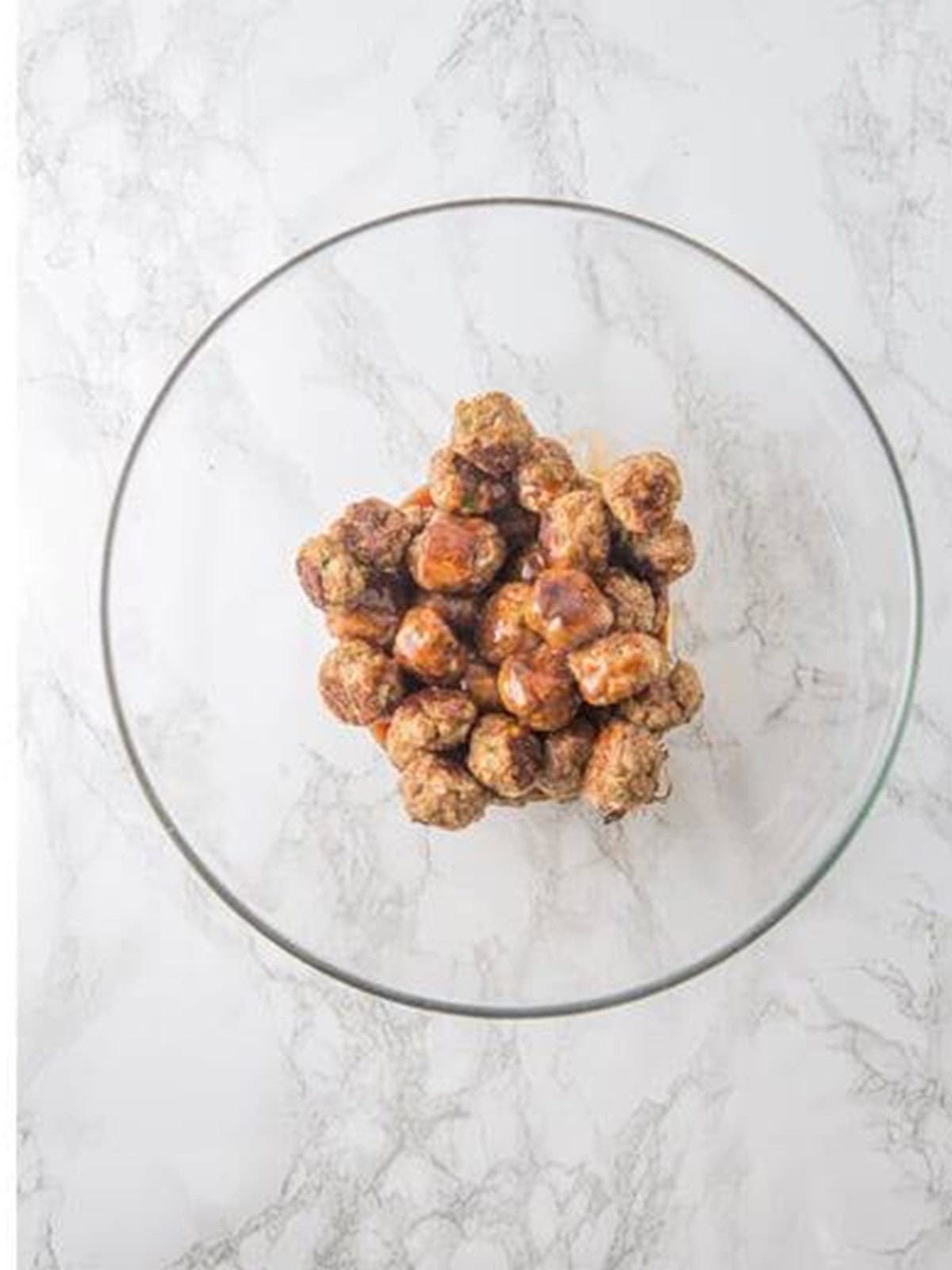 Baked meatballs tossed in honey BBQ sauce in a glass bowl.