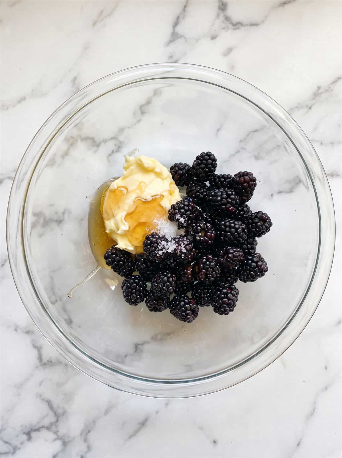 Softened butter, fresh blackberries, honey, and salt in a glass bowl before whipping into honey butter.