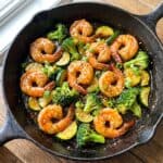 Honey garlic shrimp stir fry with broccoli and zucchini in a glossy sauce in a skillet.