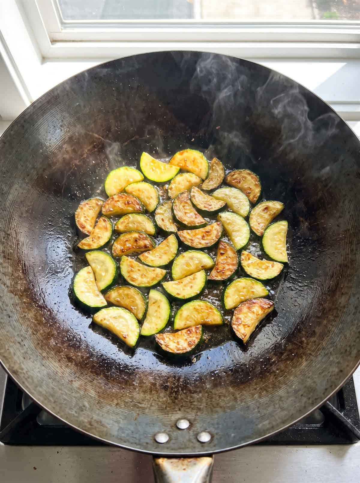 Sliced zucchini searing in a wok.