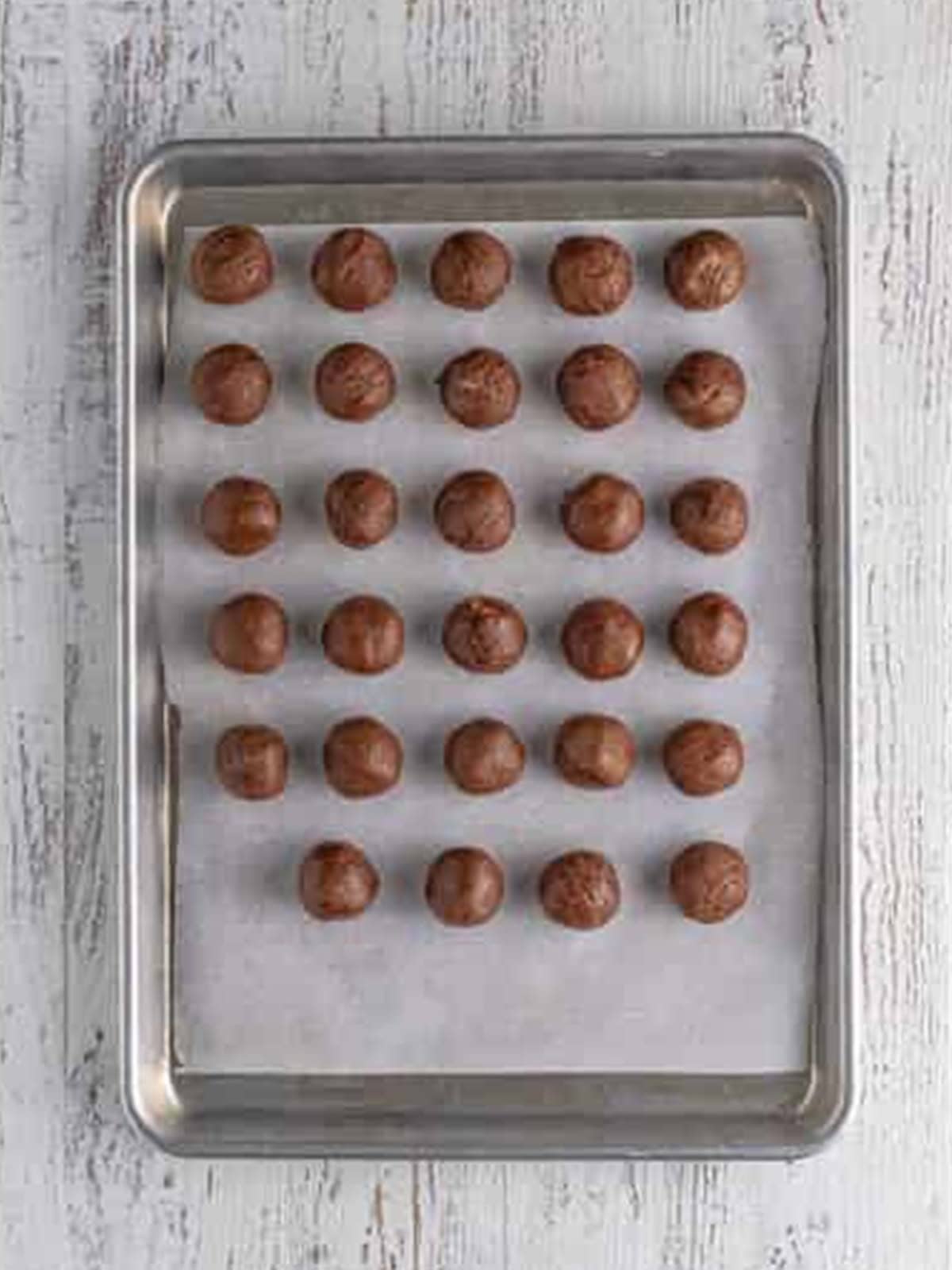 Cookie dough balls rolled and placed on a parchment-lined baking sheet.