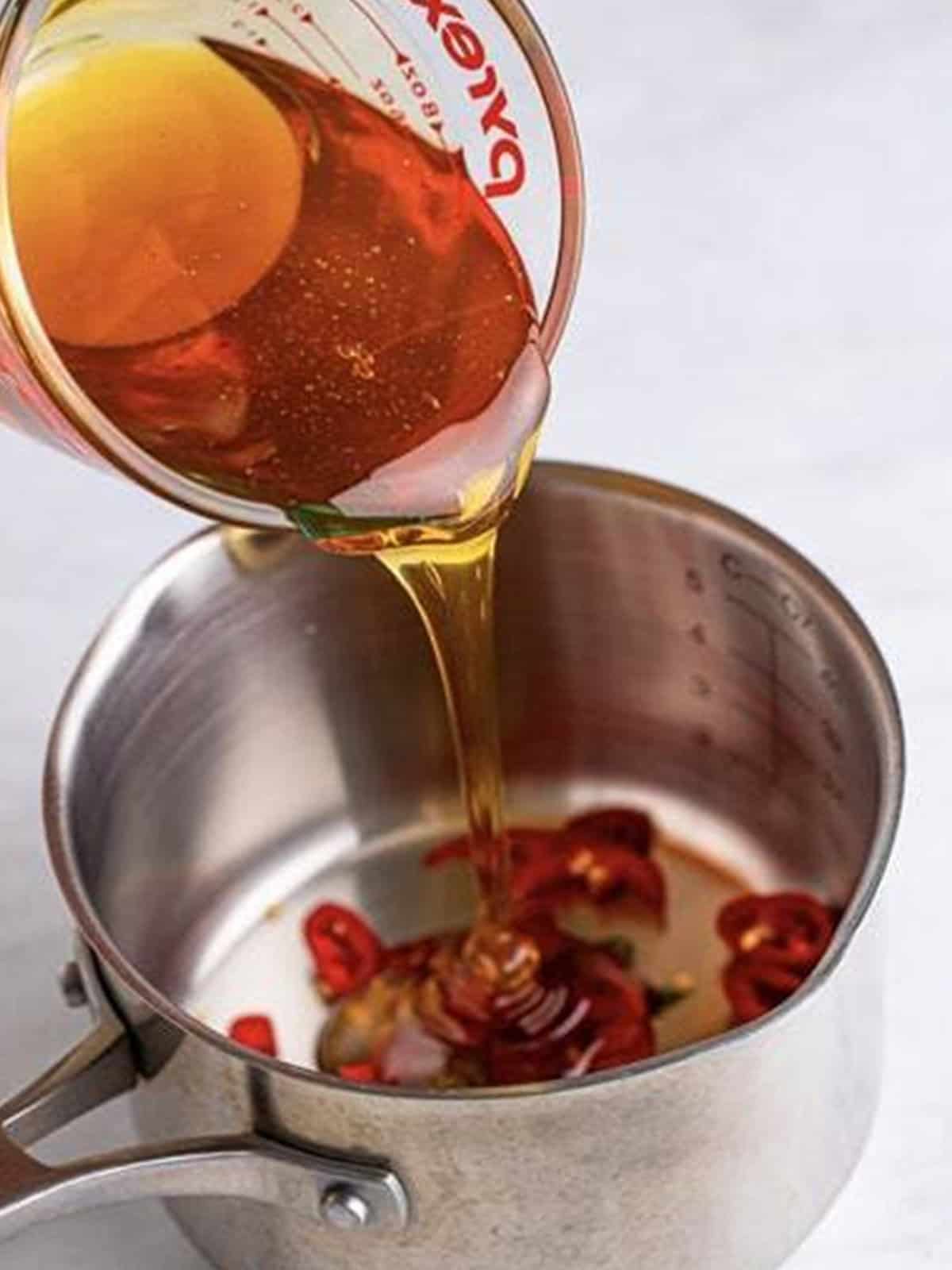 Honey poured over sliced Fresno and Thai chiles in a saucepot for Hot Honey Chicken.