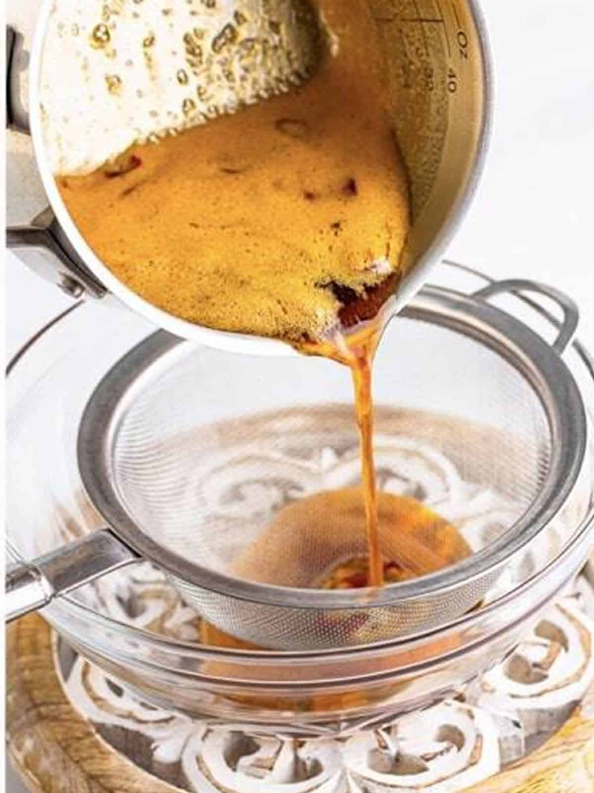 Simmered hot honey poured through a fine mesh strainer for Hot Honey Chicken.