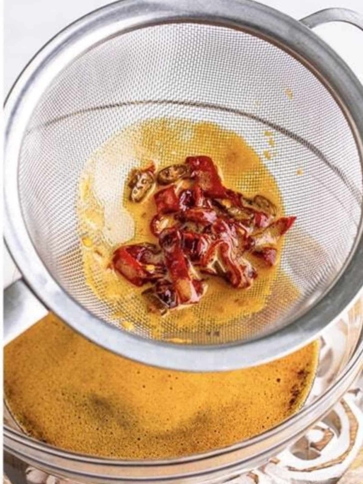 Strained chiles in a mesh strainer over a bowl of hot honey for Hot Honey Chicken.