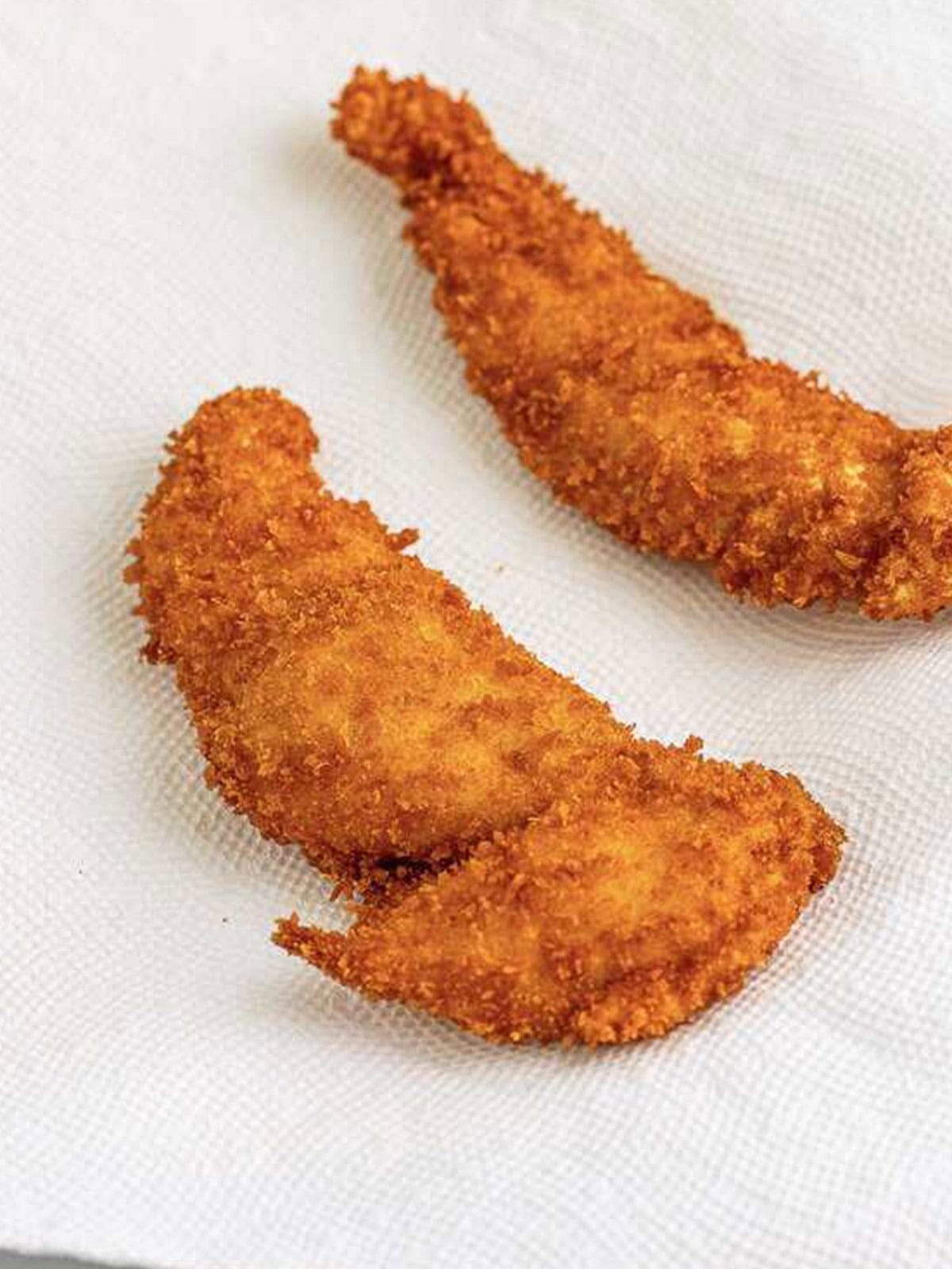 Golden fried Hot Honey Chicken tenders draining on a paper towel.