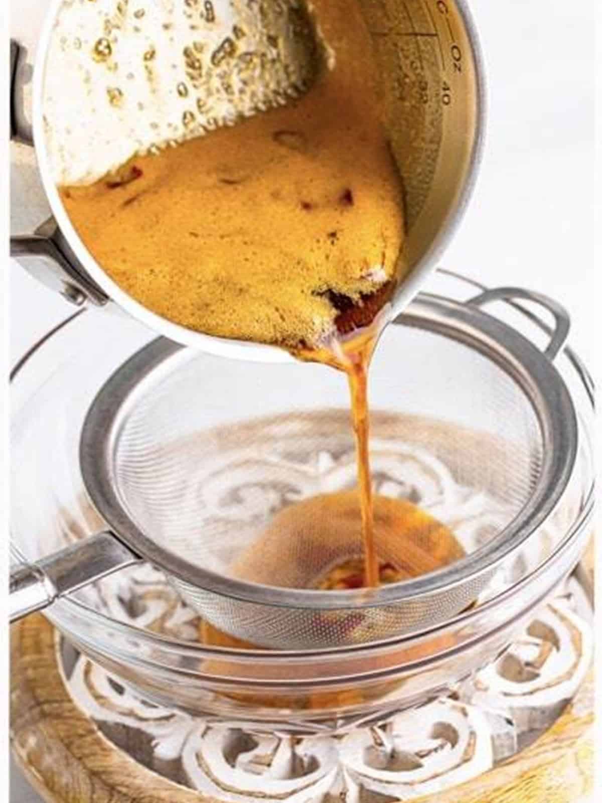 Simmered hot honey being poured through a fine mesh strainer.