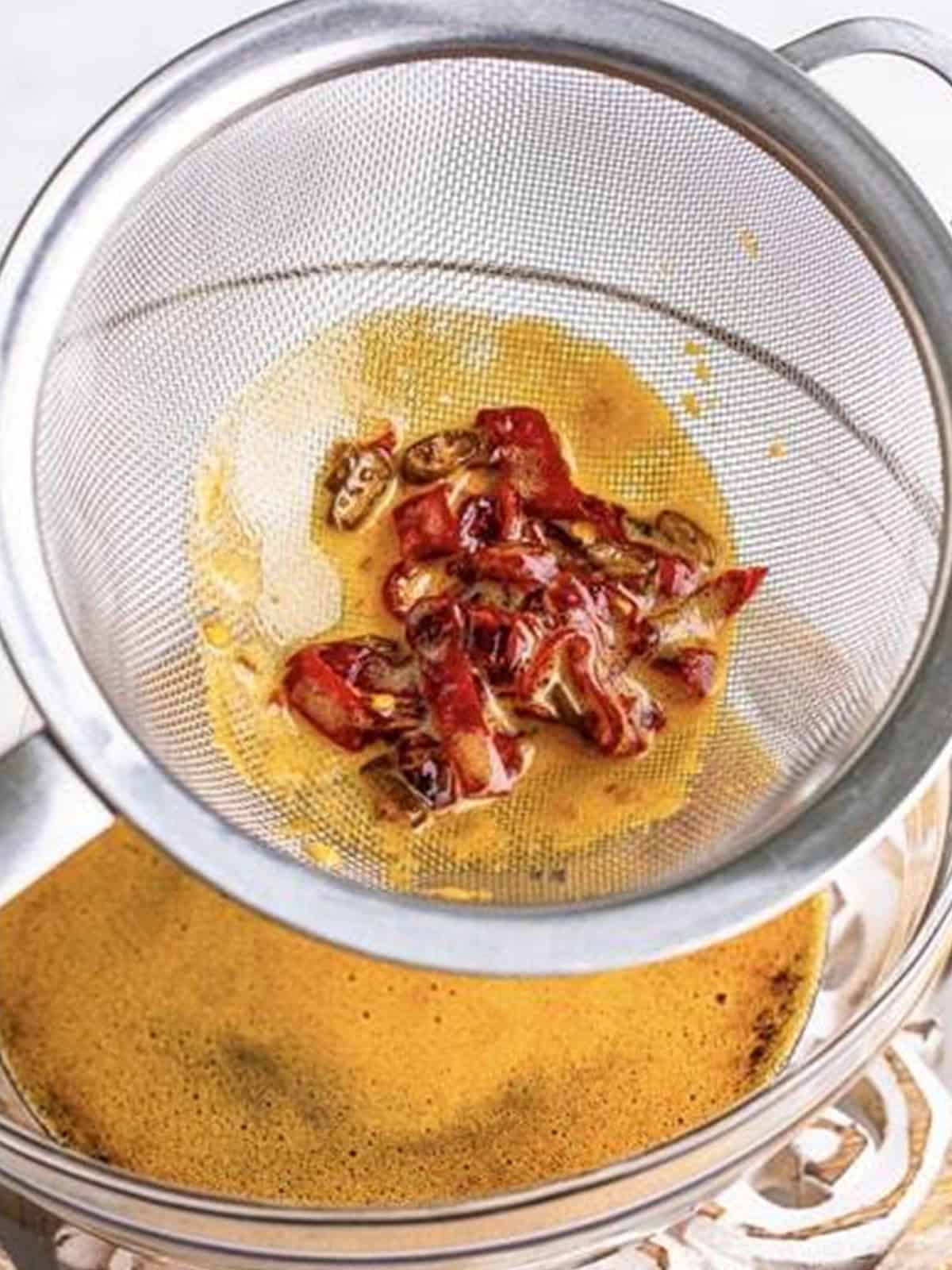 Chiles strained out of the hot honey in a mesh strainer over a bowl.