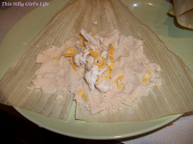 Masa spread on a corn husk topped with shredded chicken filling to make tamales.