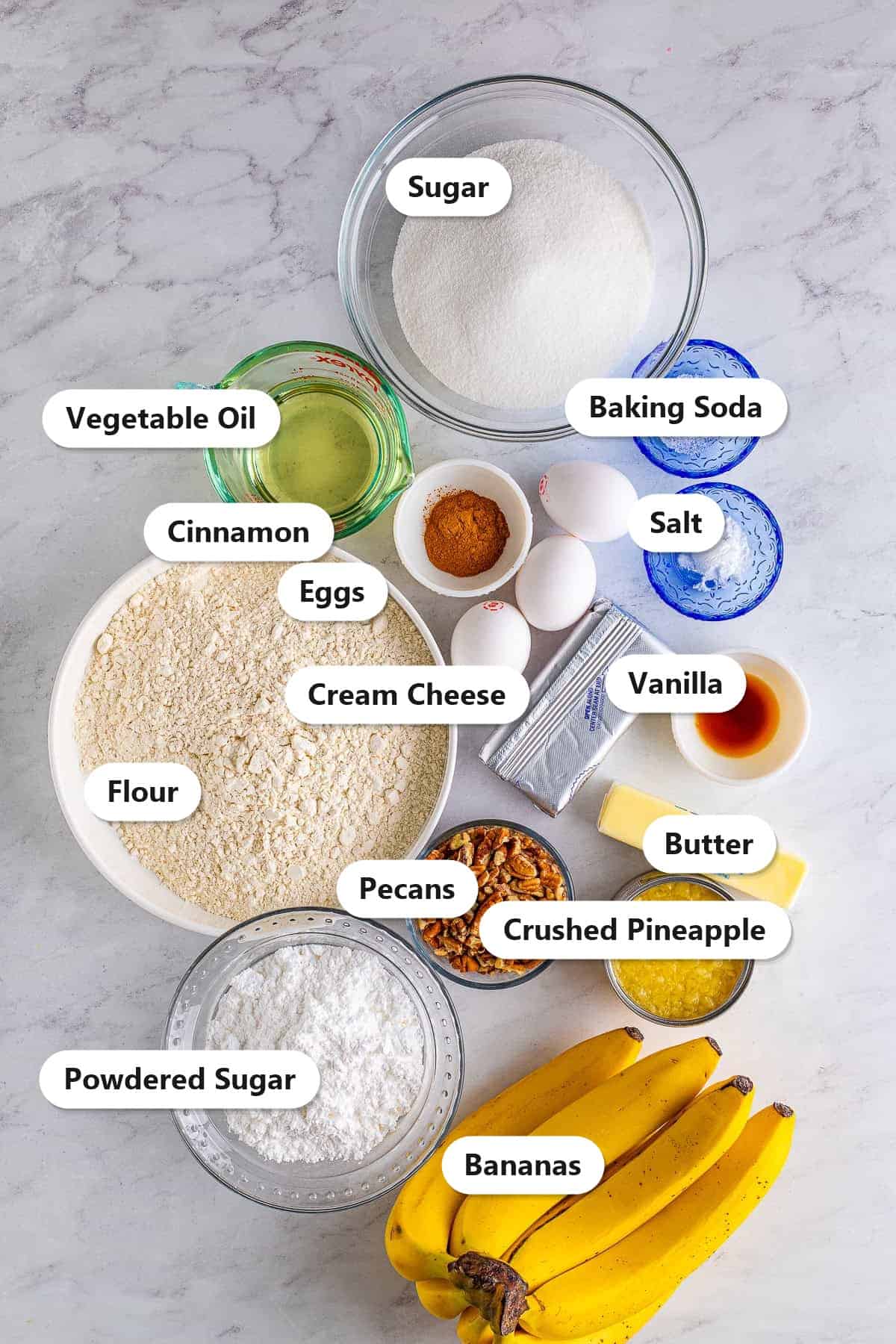 Labeled ingredients for Hummingbird Cake including flour, sugar, vegetable oil, eggs, mashed banana, crushed pineapple, pecans, and cream cheese.