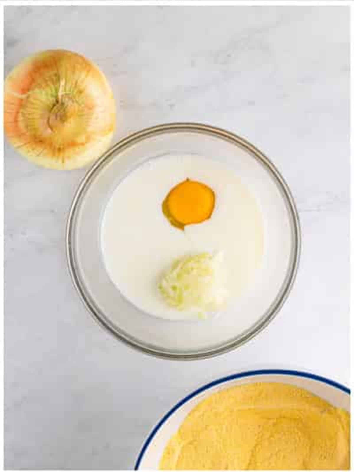 Buttermilk, egg, and grated onion in a bowl for hush puppy recipe.