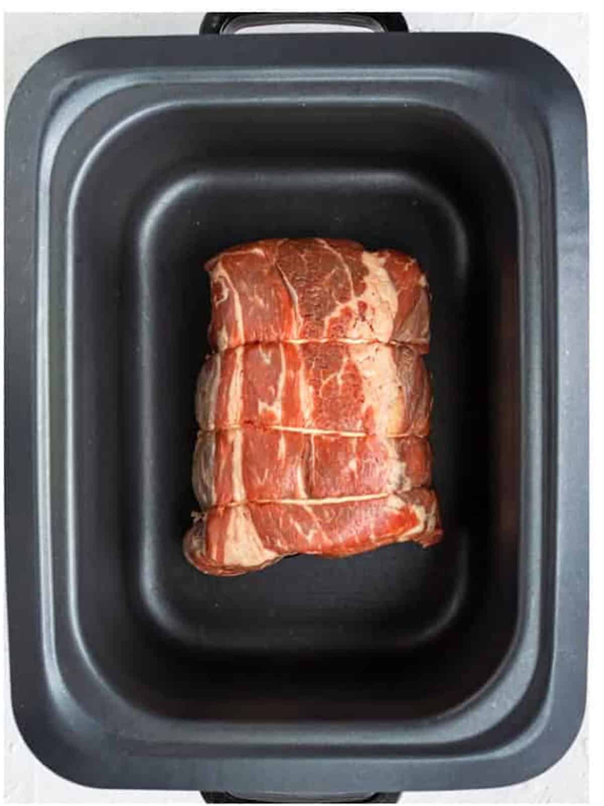 A chuck roast placed in the slow cooker for Italian beef sandwiches.