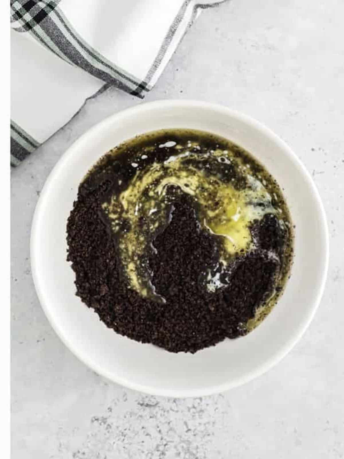 Melted butter poured over half of the Oreo crumbs in a bowl.