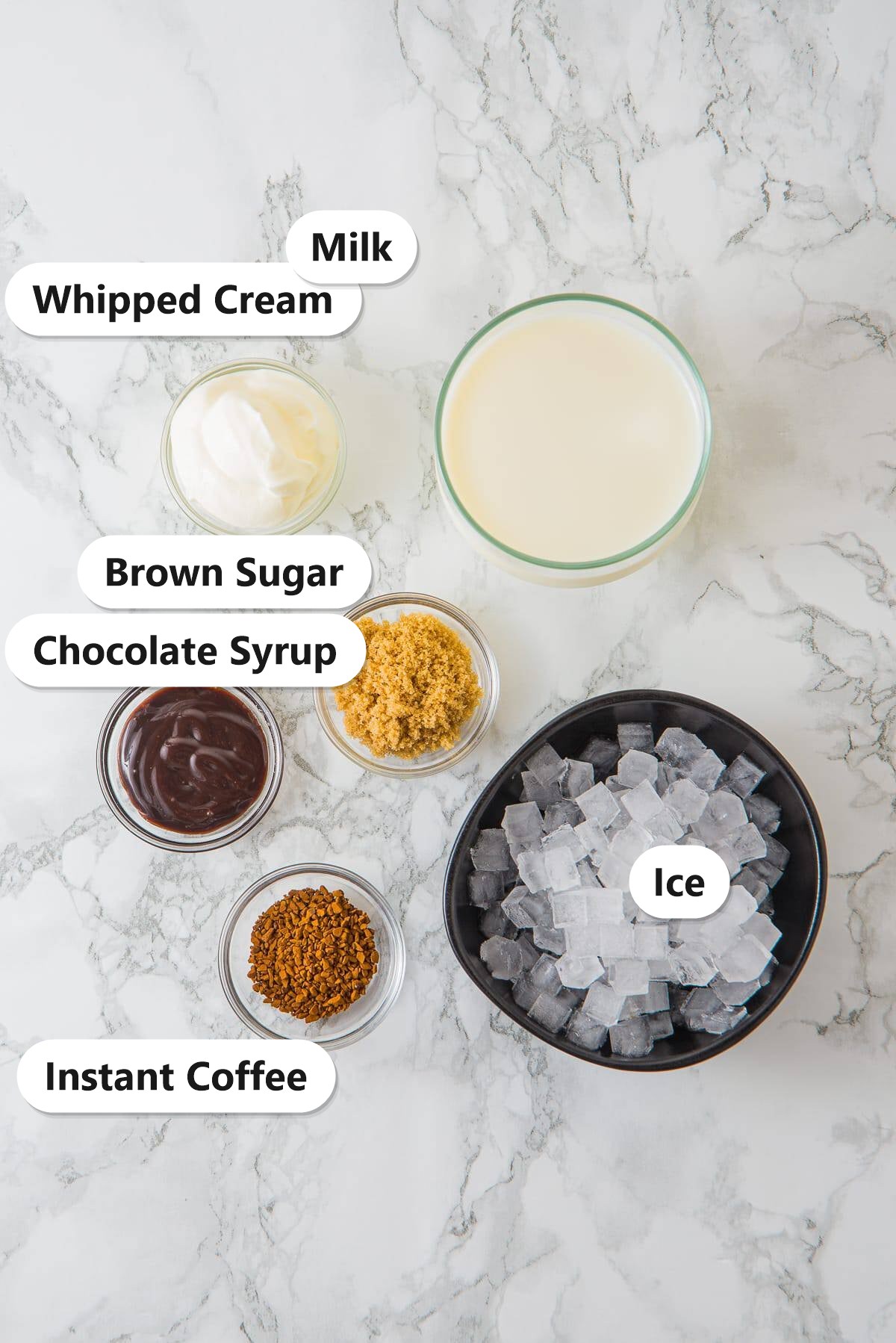 Iced Mocha ingredients including instant coffee, brown sugar, chocolate syrup, milk, ice, and whipped cream labeled on a marble counter.