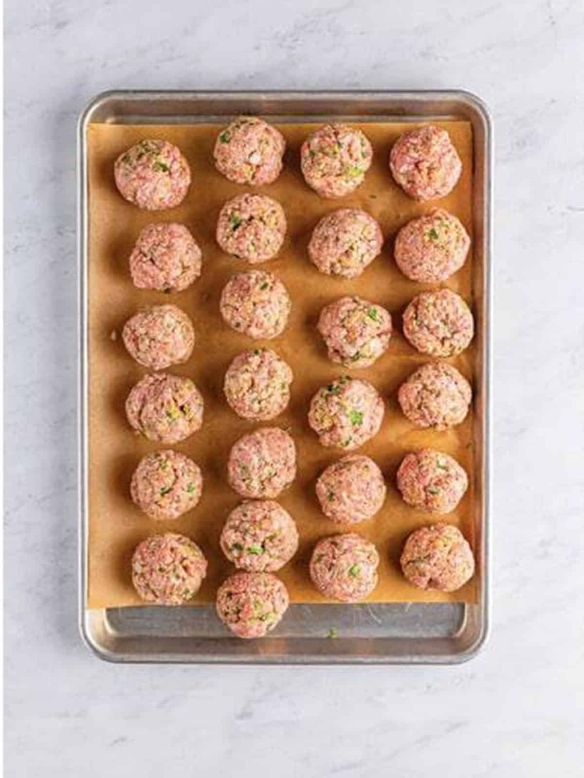 Raw Italian meatballs rolled and placed on a parchment-lined tray.