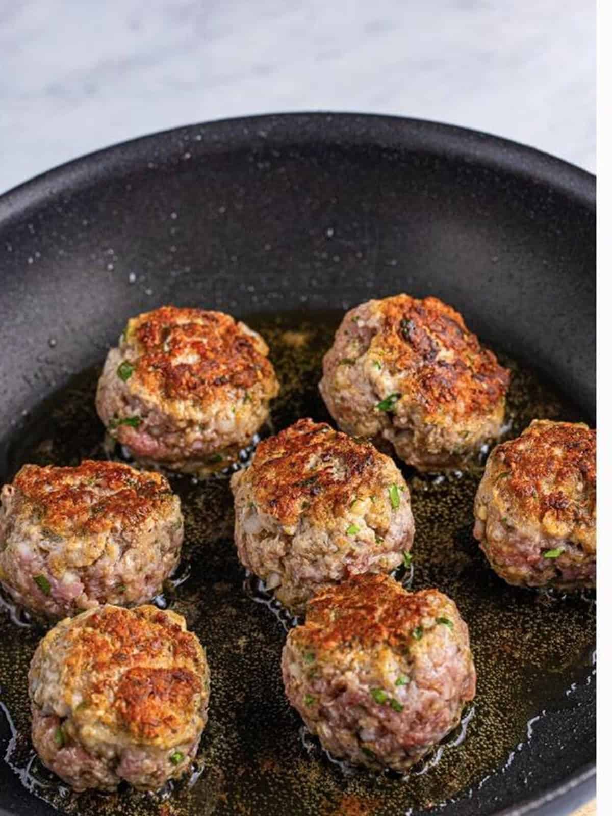 Italian meatballs frying until golden brown in a skillet.