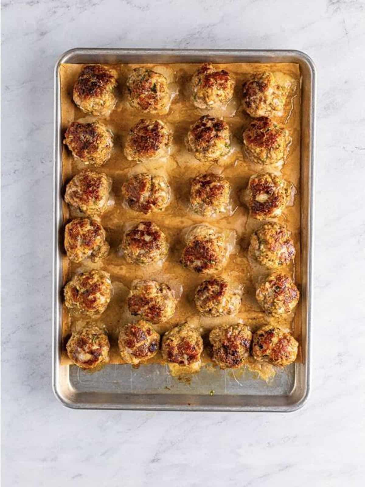 Browned Italian meatballs placed back on a sheet tray.