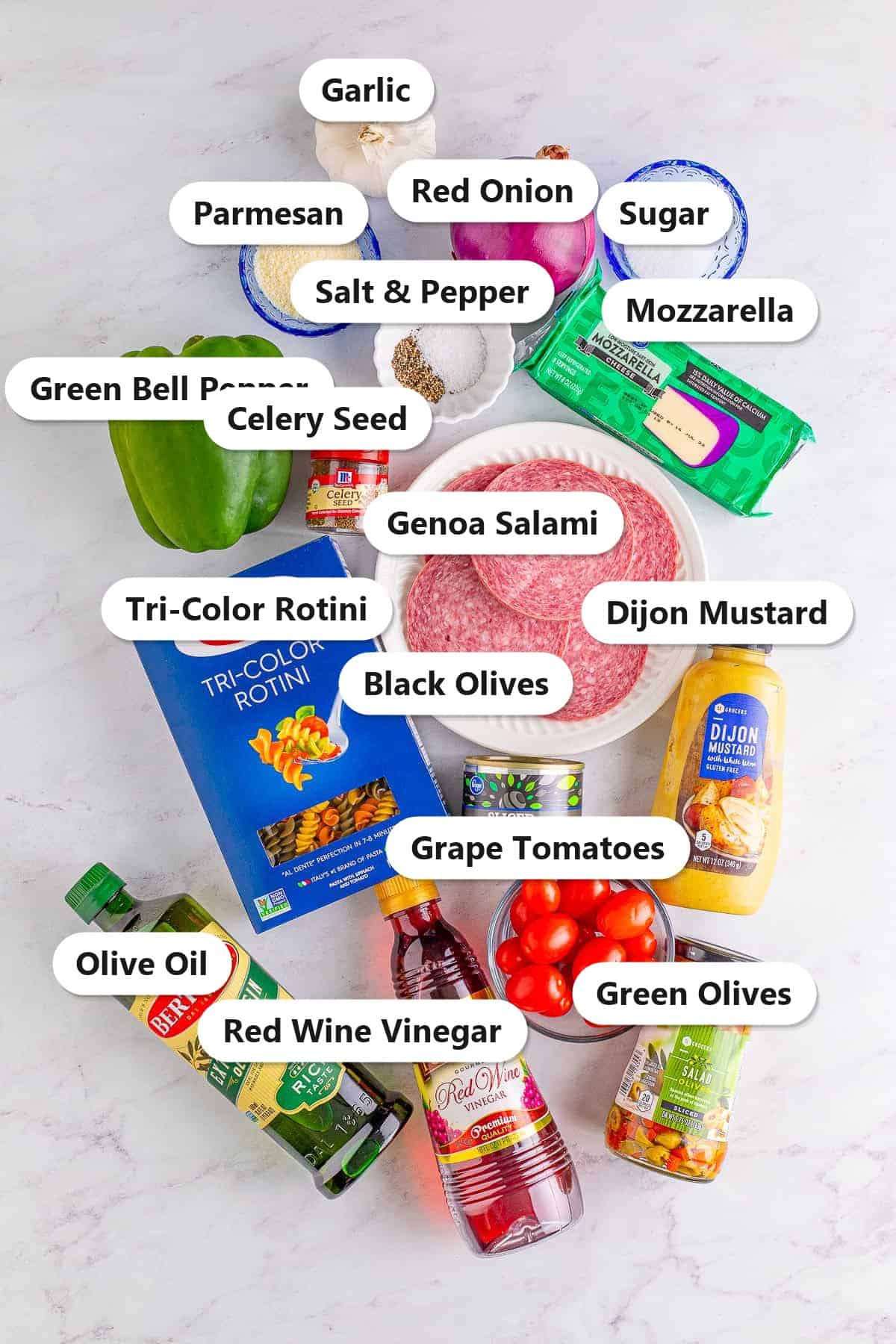 Labeled ingredients for Italian pasta salad including tri-color rotini, genoa salami, mozzarella, grape tomatoes, green bell pepper, red onion, black and green olives, olive oil, red wine vinegar, dijon mustard, parmesan, garlic, and seasonings.