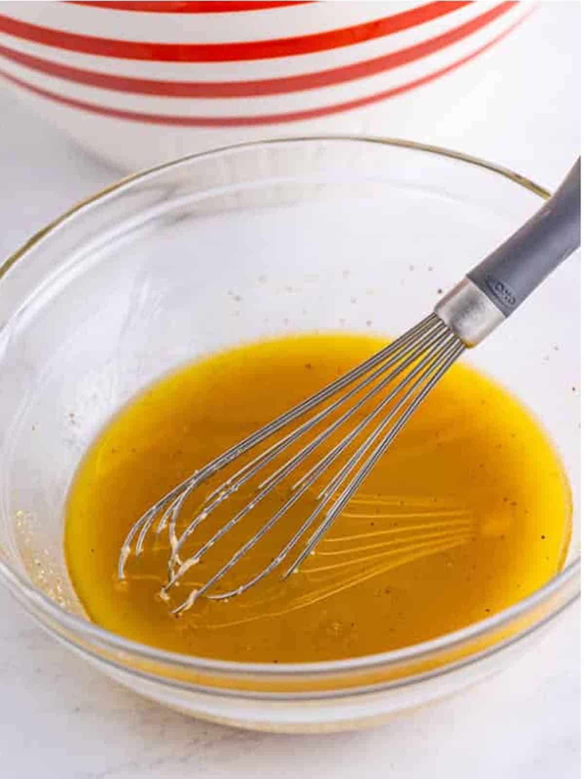 Whisking the homemade Italian dressing of olive oil, red wine vinegar, and dijon in a glass bowl.