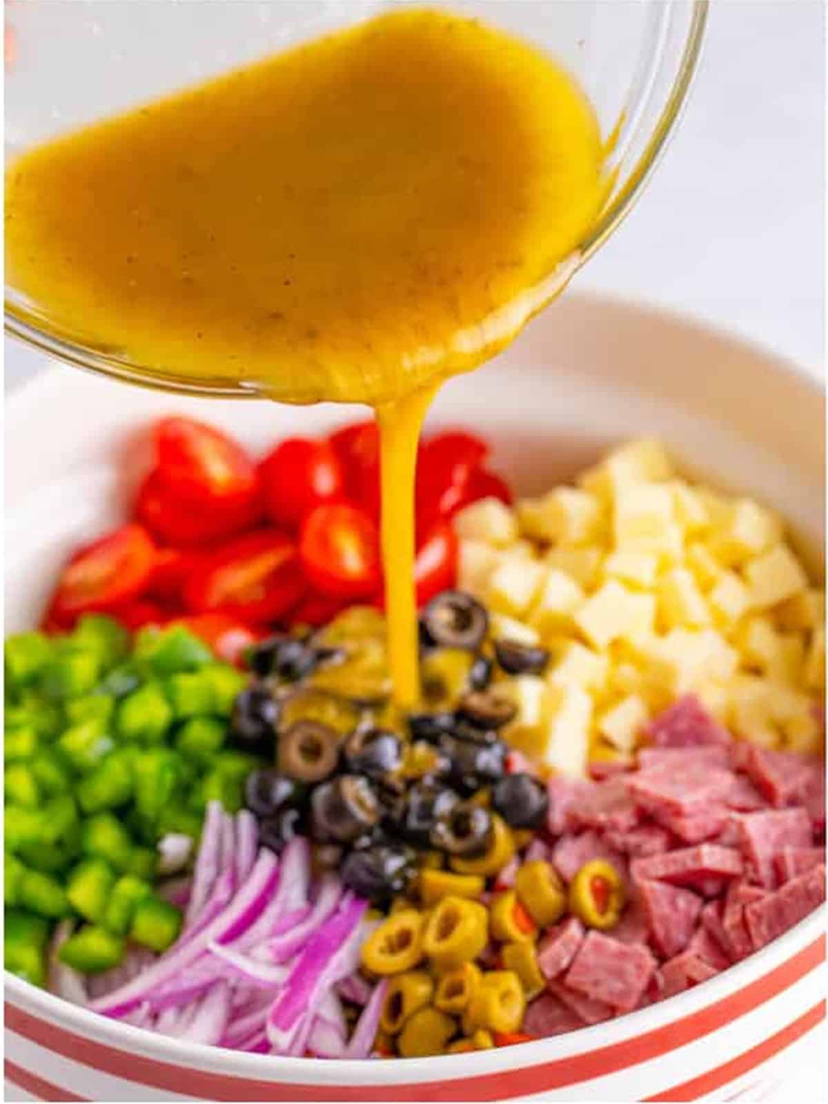 Pouring the homemade dressing over the Italian pasta salad ingredients before tossing.