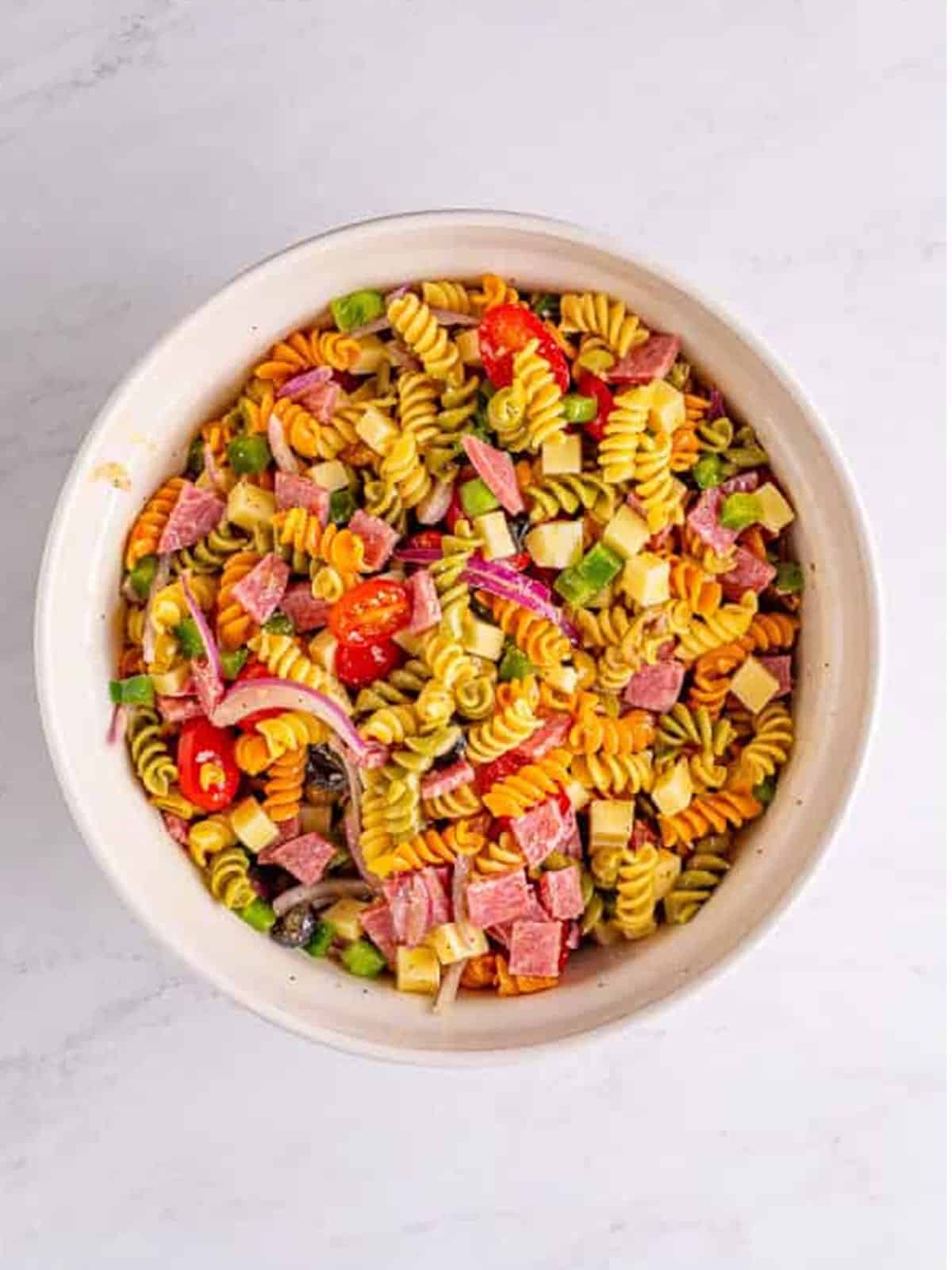 Finished Italian pasta salad tossed in dressing in a white bowl.