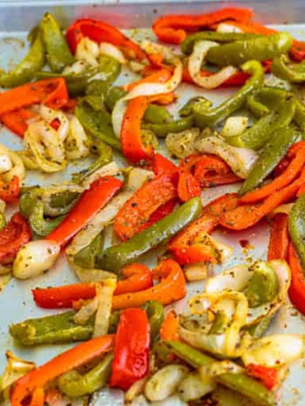 Sliced bell peppers and onions roasted on a sheet pan for Italian sausage sandwiches.
