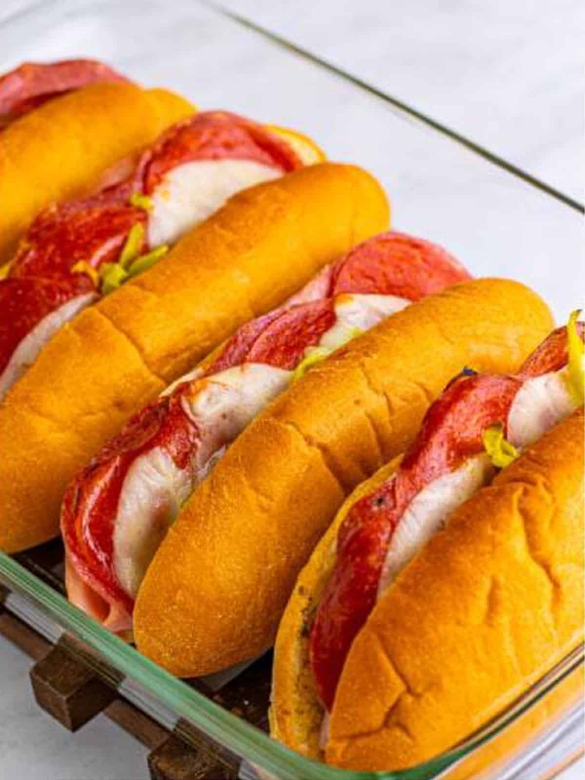 Finished baked Italian subs in a glass dish with melty cheese and golden rolls.