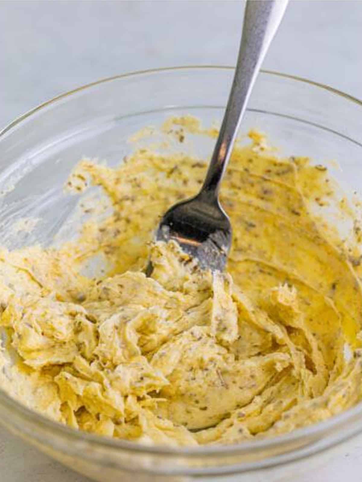 Mixing softened butter with parmesan, garlic powder, and Italian seasoning in a glass bowl.