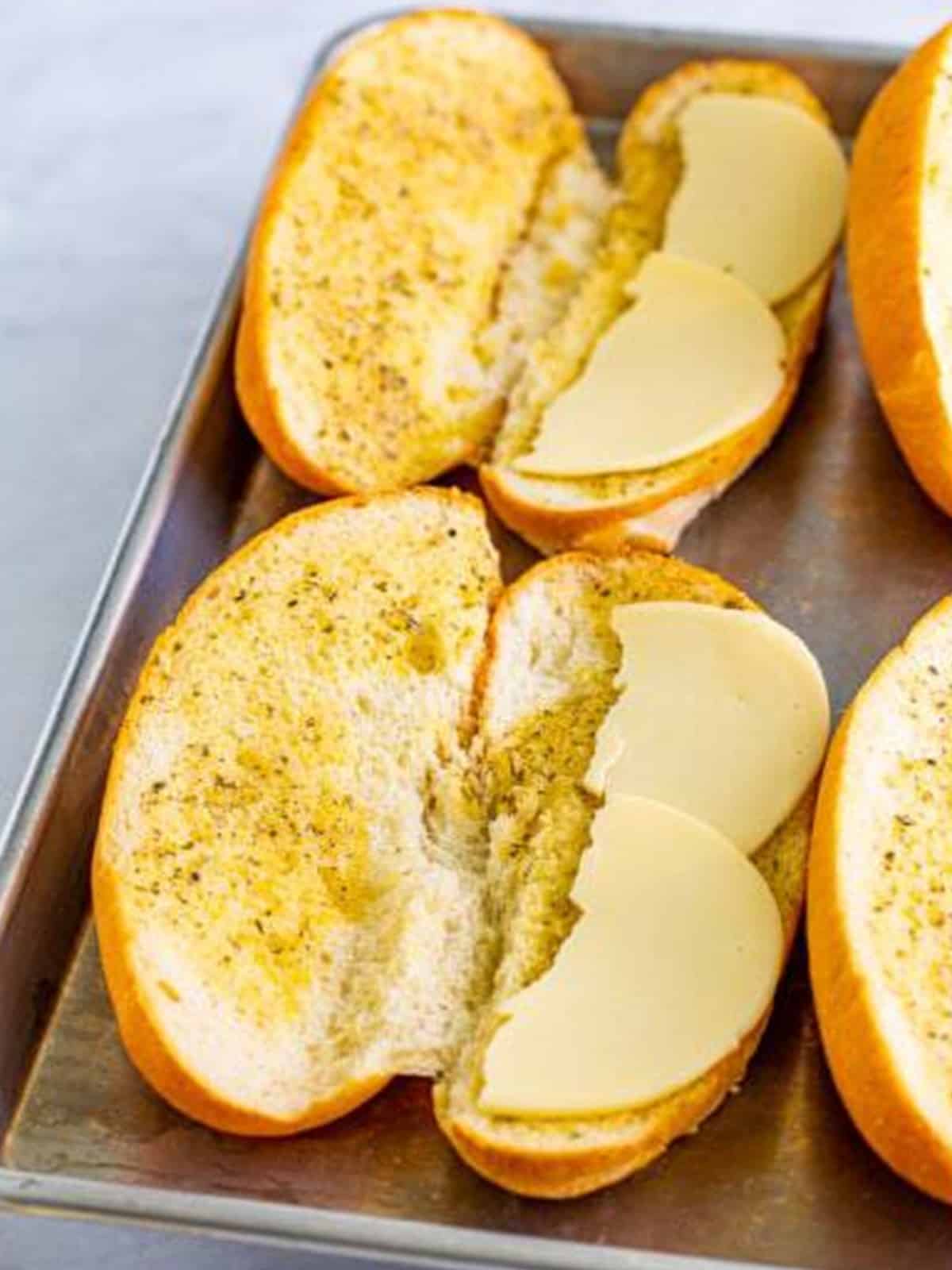 Layering provolone cheese onto the toasted hoagie rolls.