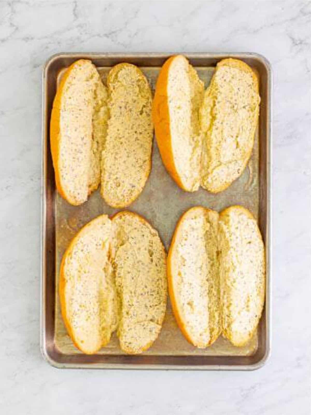 Hoagie rolls sliced lengthwise and arranged on a baking sheet.
