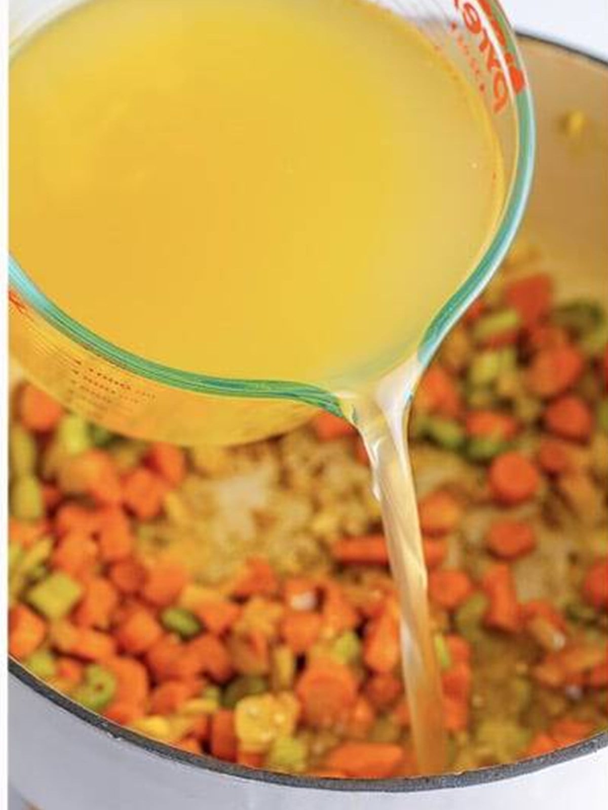 Pouring chicken broth into the pot of vegetables for Italian Wedding Soup.