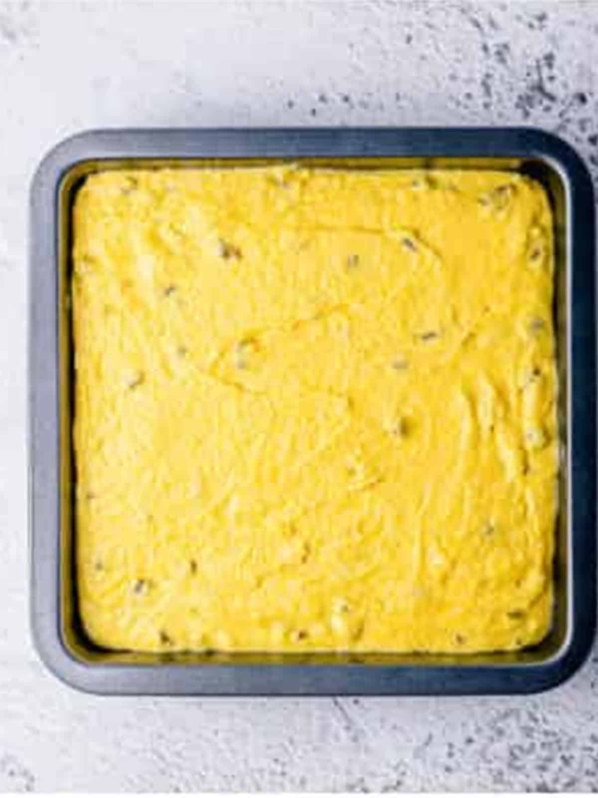 Jalapeno cornbread batter spread evenly into a parchment-lined baking dish.