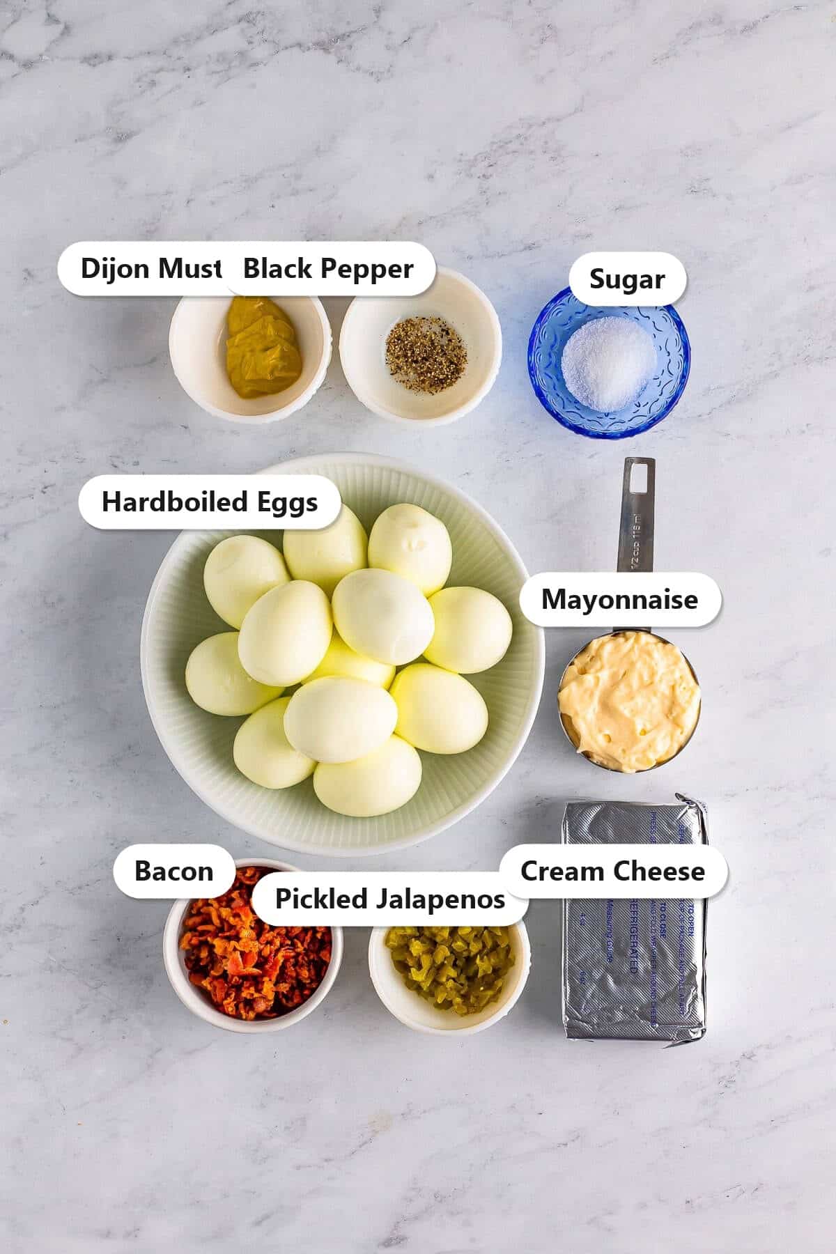 Labeled ingredients for jalapeno deviled eggs including hardboiled eggs, mayonnaise, cream cheese, pickled jalapenos, bacon, and dijon.