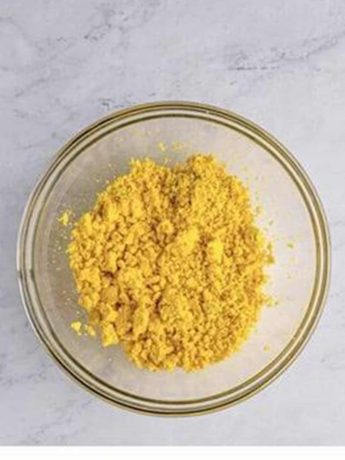 Mashed hardboiled egg yolks crumbled in a glass bowl.