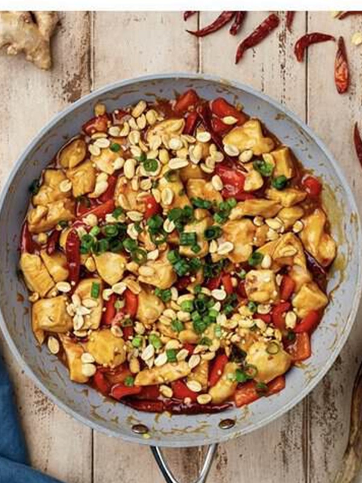 Stirring kung pao sauce, peanuts, and green onions into the chicken.