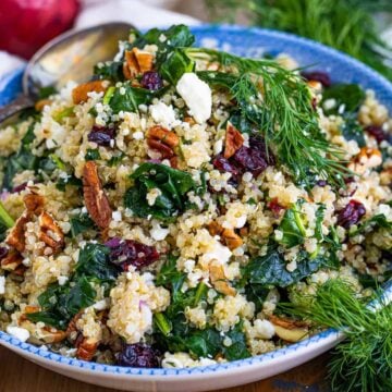 A bowl of kale and quinoa salad with cranberries, pecans, feta, and fresh dill.
