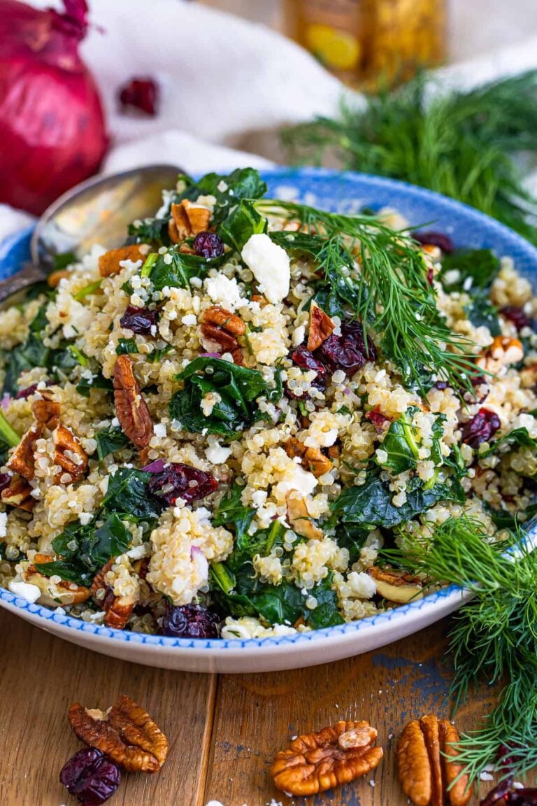 A bowl of kale and quinoa salad with cranberries, pecans, feta, and fresh dill.
